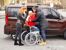 two caregivers assisting senior man to his wheelchair