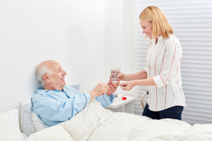 Woman gives senior in bed a tablet and a glass of water